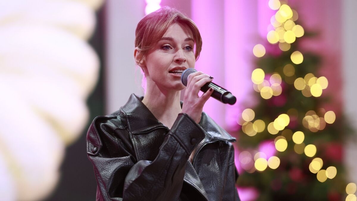 Julia Kamińska trzyma mikrofon i występuje na scenie programu „Pytanie na śniadanie”. Ubrana jest w czarną skórzaną kurtkę, a jej włosy są upięte, z luźnymi pasmami przy twarzy. W tle widać rozświetloną choinkę i różowe światło sceniczne, które nadaje ujęciu świąteczny charakter.